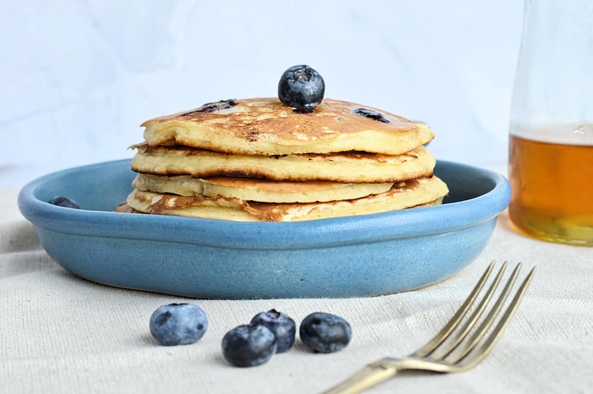 Pancakes aux bleuets dans assiette bleue avec fourchette et bleuets décoratifs.