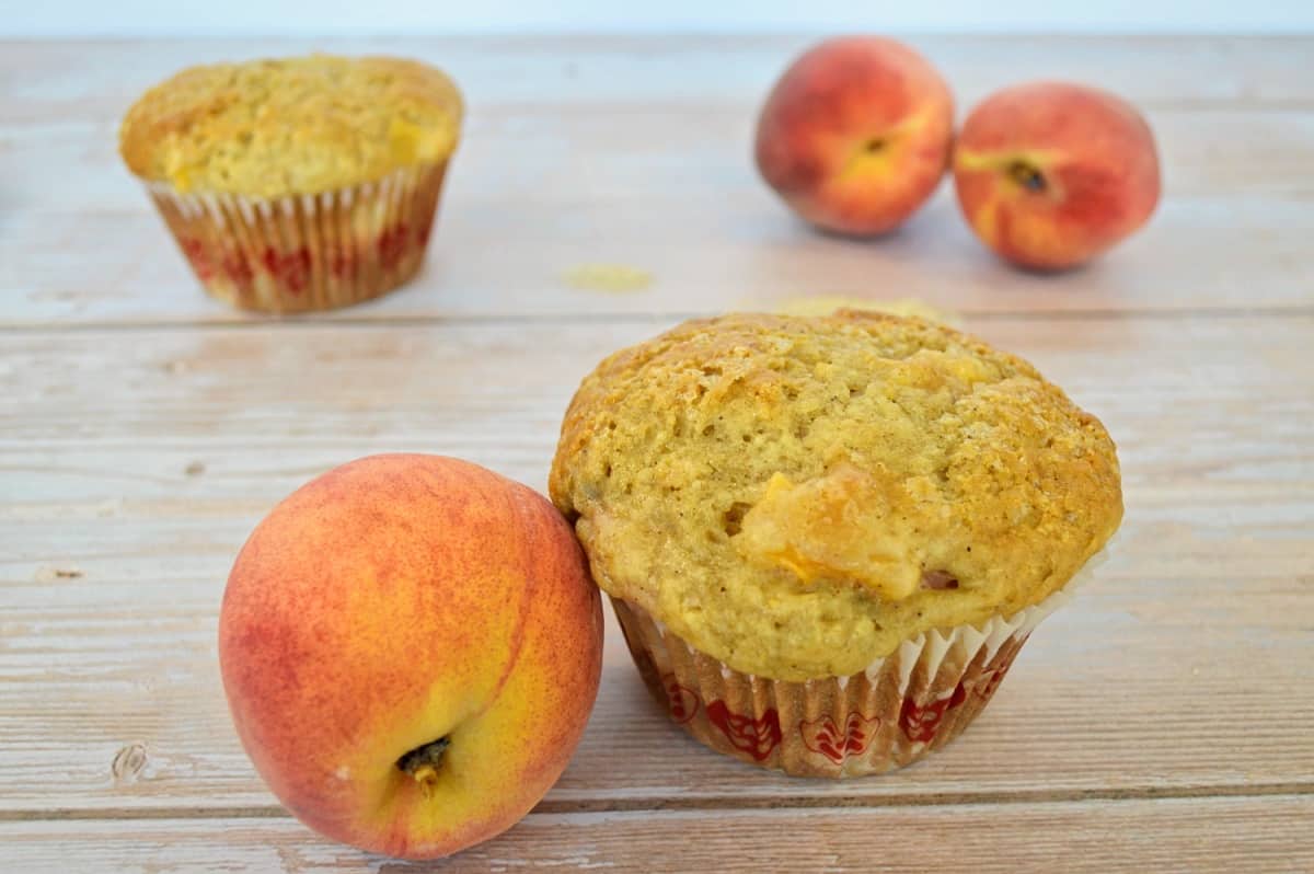 3 pêches et 2 muffins sur un fond de bois. 