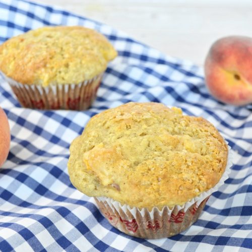 2 Muffins et 3 pêches sur une nappe carottée bleue.