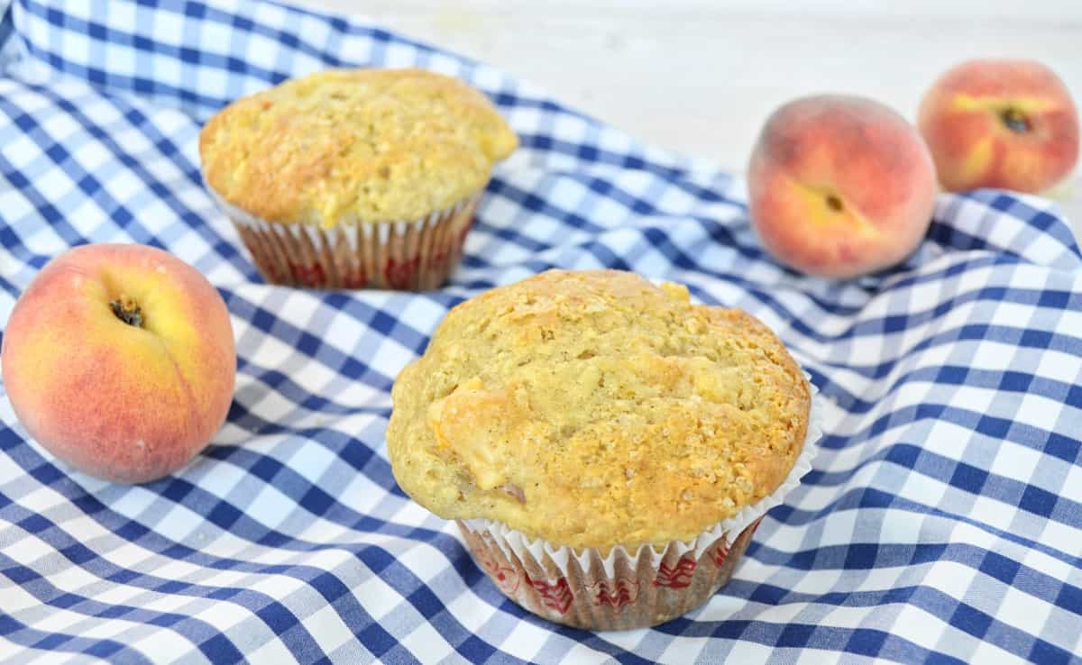 2 Muffins et 3 pêches sur une nappe carottée bleue.