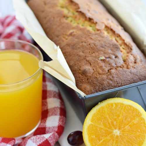 Gâteau cuit dans un moule à pain avec un verre de jus d'orange et une orange devant.