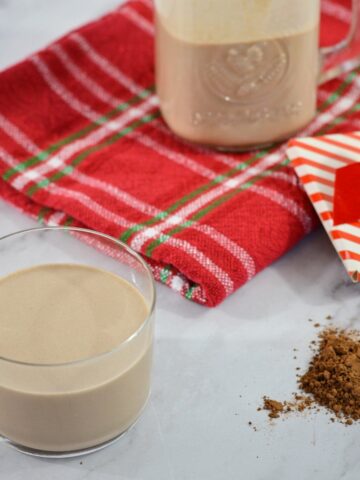 Un verre de Baileys maison avec de la poudre de cacao, un serviette de table et un contenant de baileys.