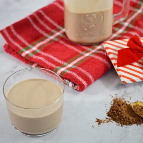 Un verre de Baileys maison avec de la poudre de cacao, un serviette de table et un contenant de baileys.